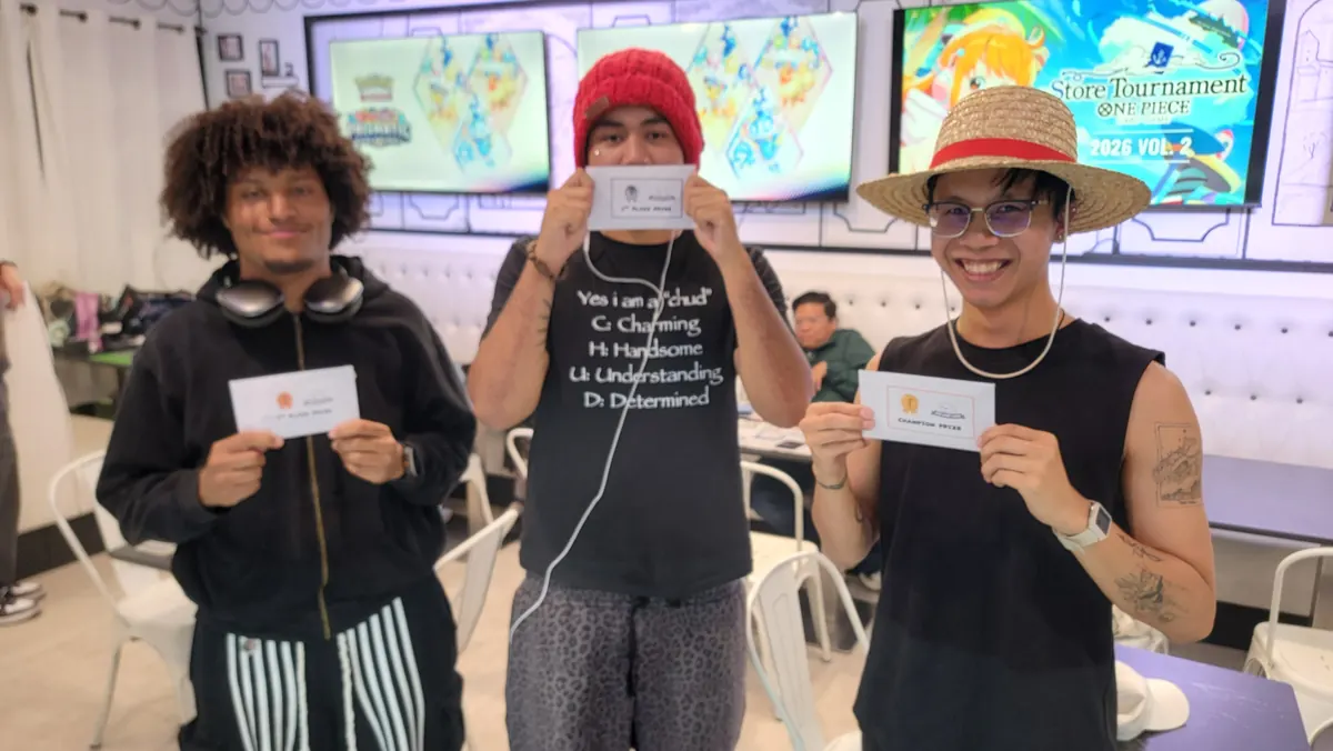 Three players holding prize envelopes in front of the One Piece store tournament screens