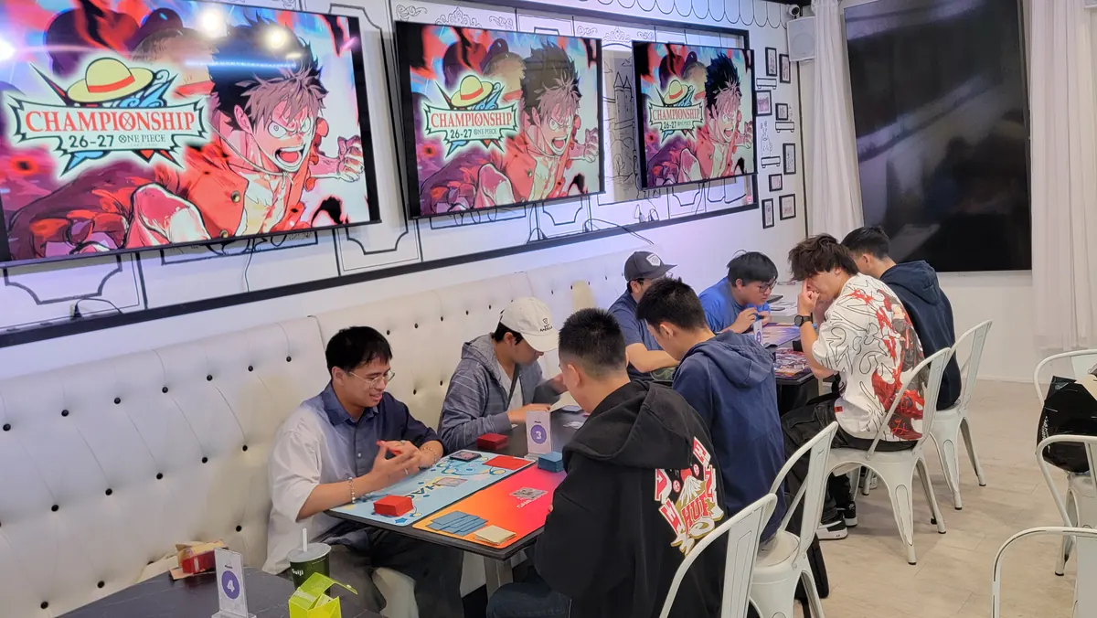 One Piece Championship 26-27 night at Arcane Maid Café, players at long tables under Luffy art on the TVs