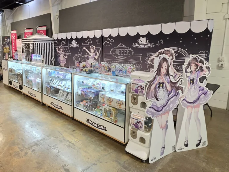 Arcane Maid Café shop display cases full of TCG products and goodies, with an awning backdrop and maid standees