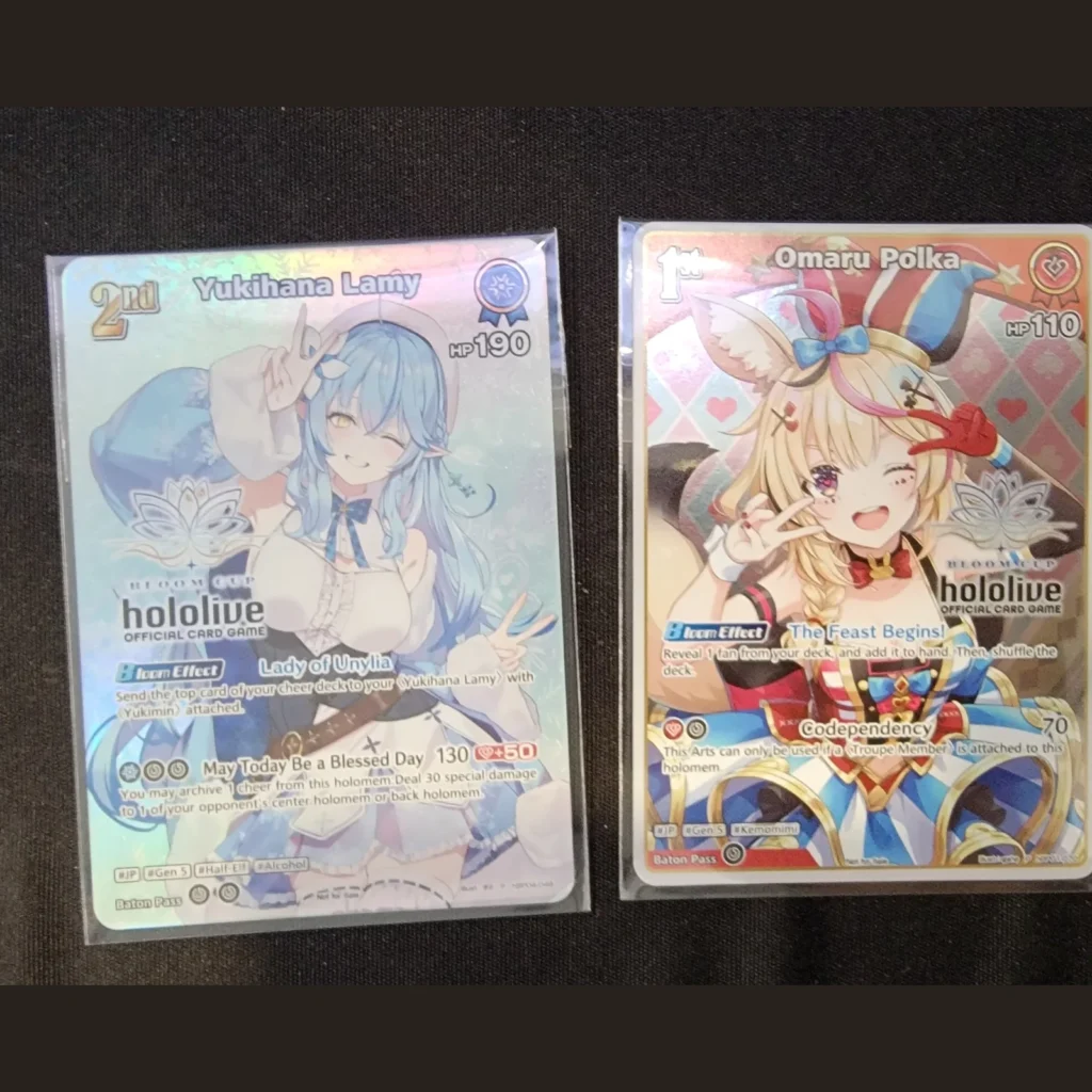 hololive OCG Bloom Cup promo cards of Yukihana Lamy (2nd) and Omaru Polka (1st), square crop, at Arcane Maid Café